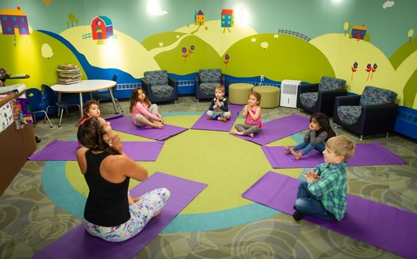 A teacher and children sitting in a circle on yoga mats doing yoga